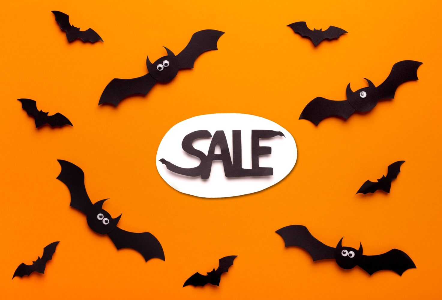 Flying paper bats on orange background with promo text